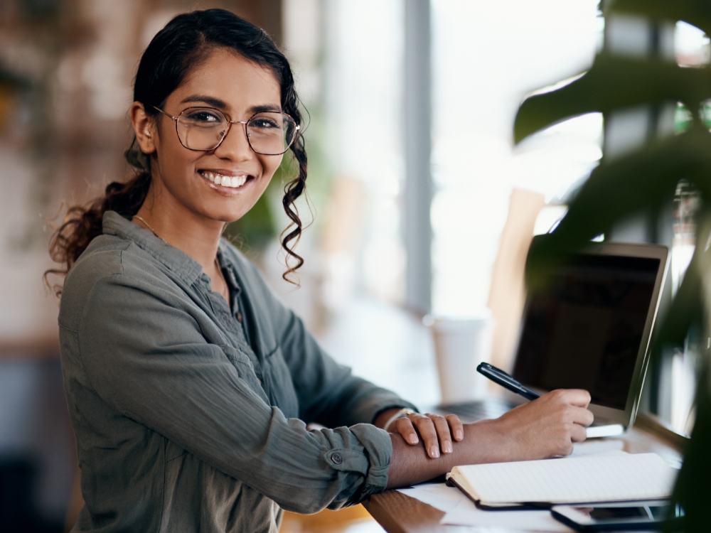 Smiling person working on a laptop in a relaxed, modern workspace, representing a flexible and positive work environment.